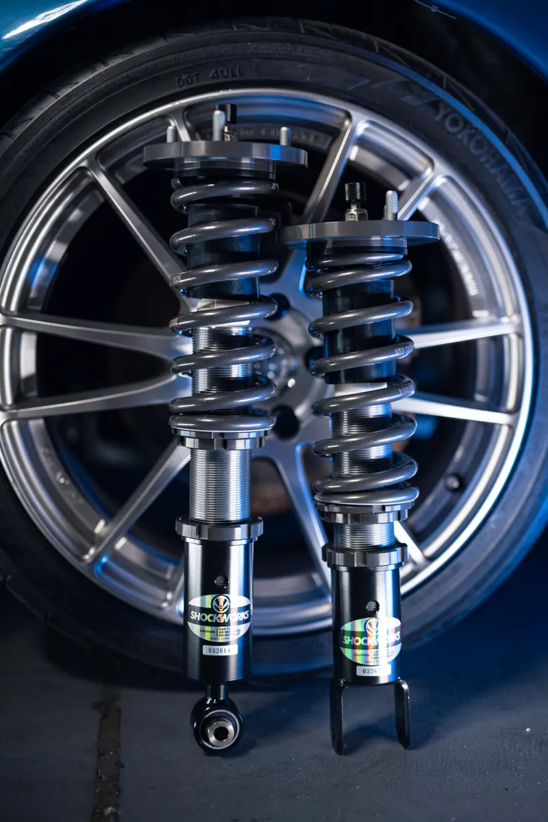A pair of assembled Shockworks coilovers standing upright in front of an alloy wheel