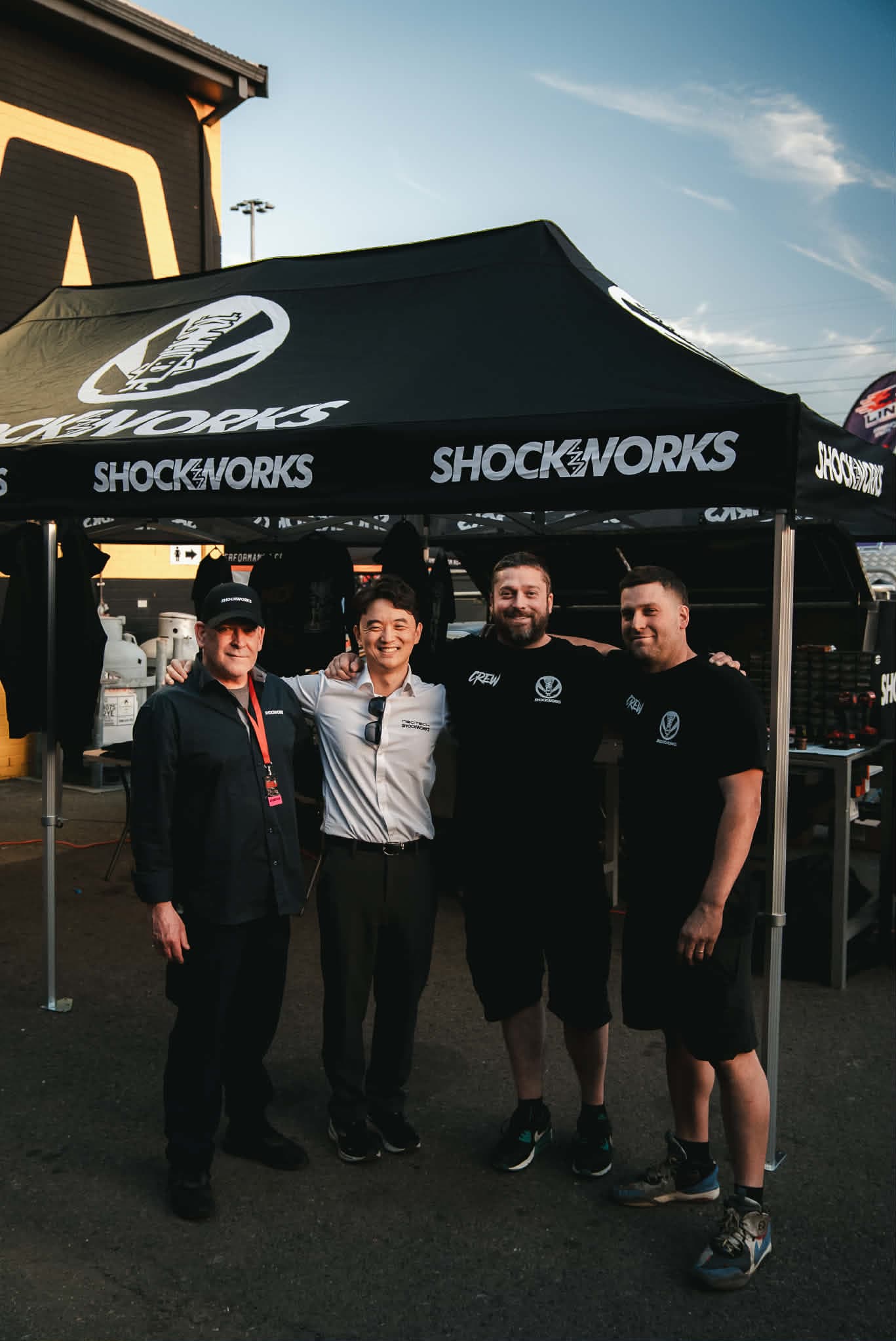 Four of the Shockworks crew arm in arm under the black Shockworks marquee at a race event