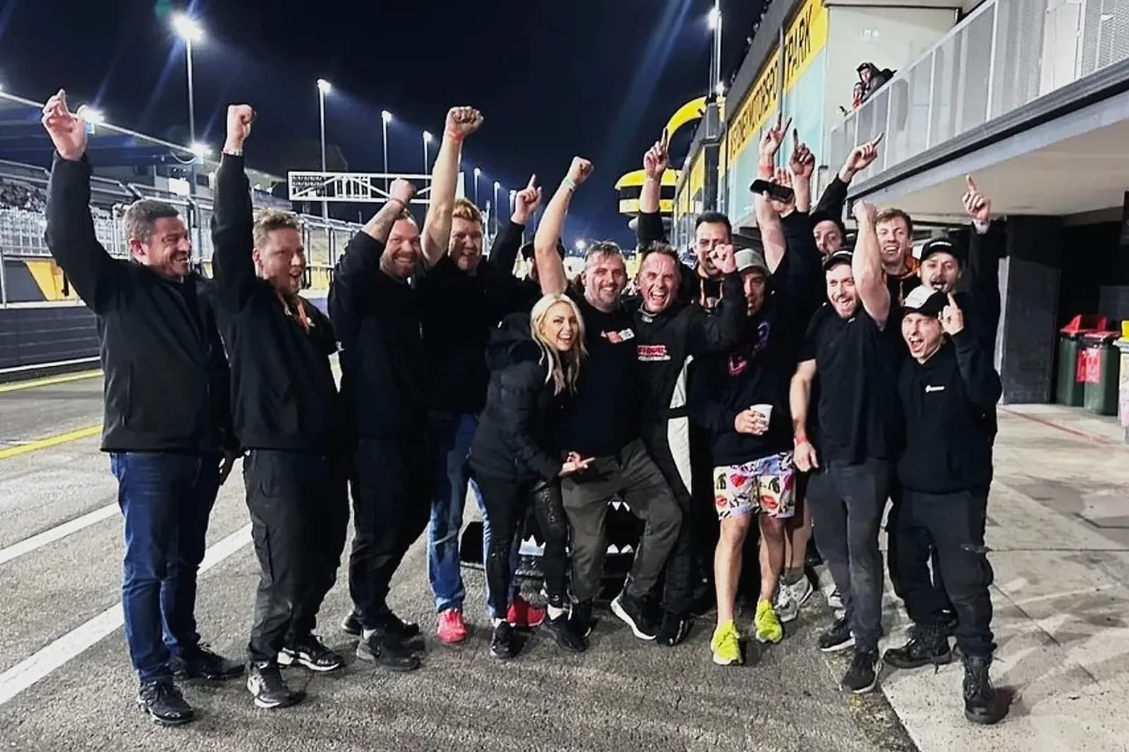 JET200's driver and crew in pit lane at night with their arms in the air, the pit building lit behind them