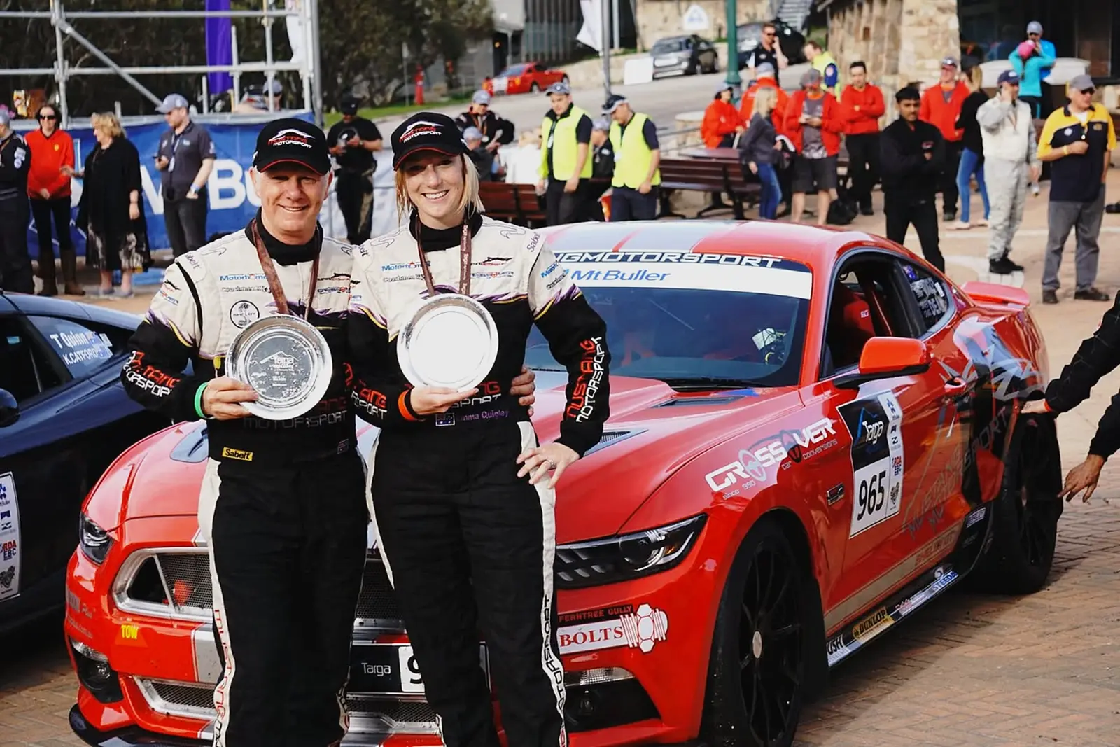 The red Mustang Motorsport Targa car, number 965, at Mt Buller with its two drivers holding trophies