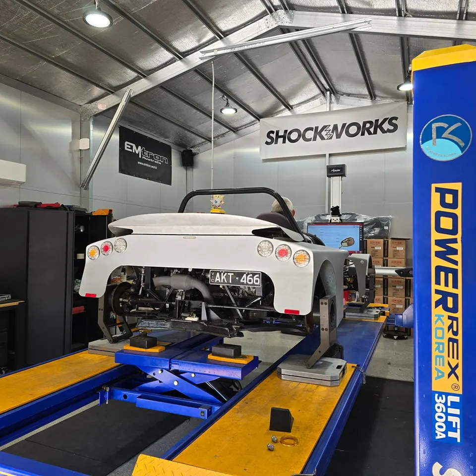 The bare-aluminium open-top on the alignment lift, rear-on under the Shockworks banner, alignment gear on the bench behind